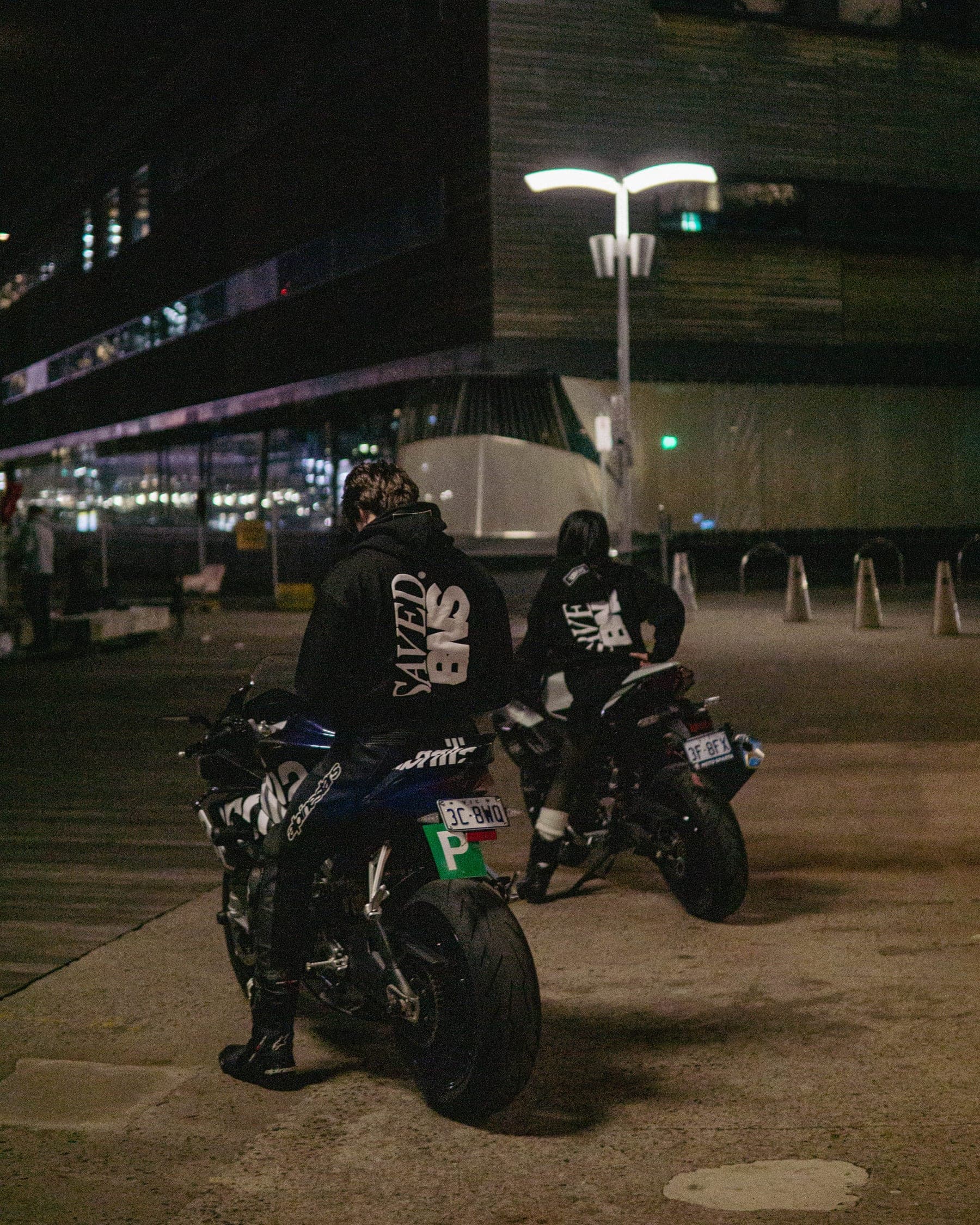 The two riders from behind under a streetlight, the back print lit against the dark